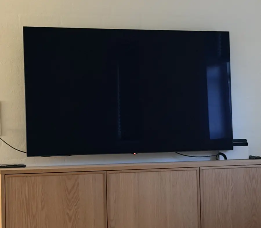 An LG TV on a wooden sideboard, screen dark, standby light showing red